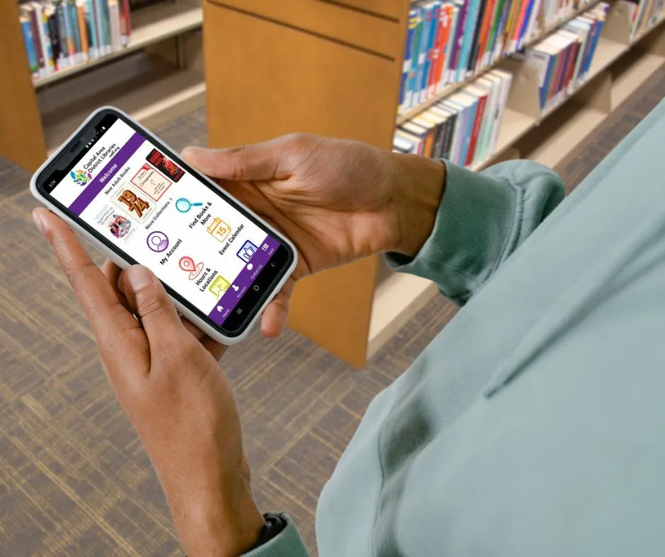 Capital Area District Libraries mobile app being used inside a library, with My Account and library services visible
