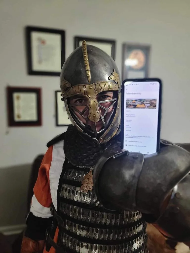 Society for Creative Anachronism member in historical armour presenting a digital membership card on a phone